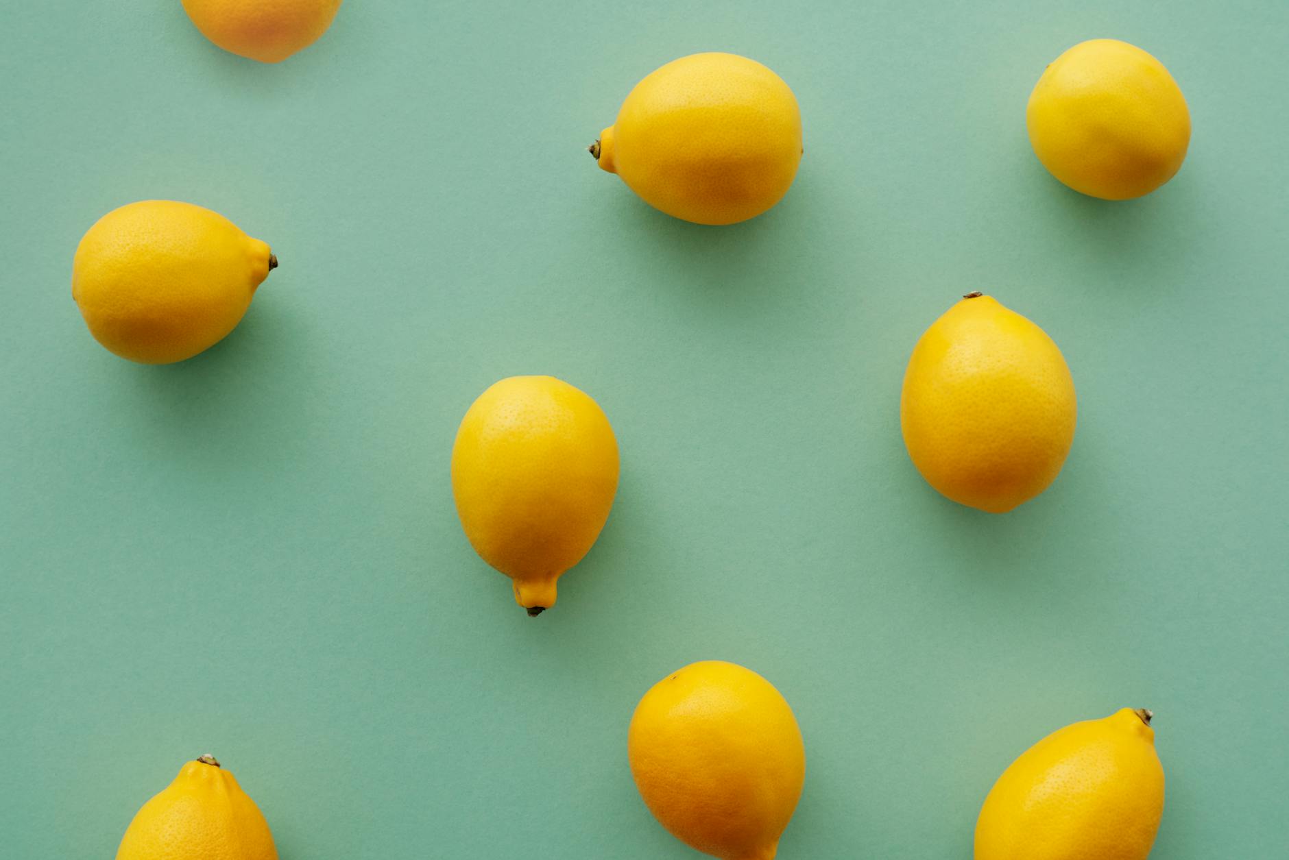 Hand holding a fresh lemon on soft pink background surrounded by additional lemons