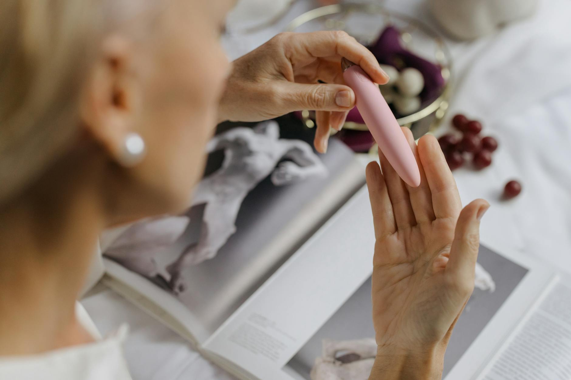 Close-up of a hand holding a pink vibrator with art books in the background, symbolizing personal healing and reconnection with pleasure
