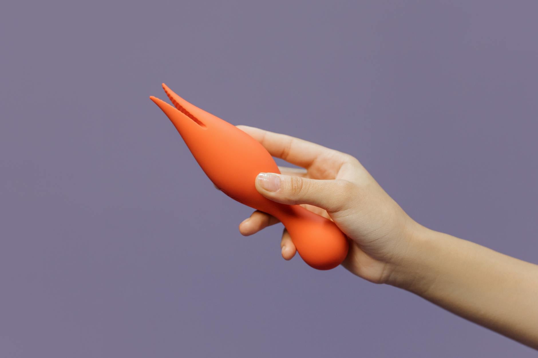 A hand holding a bright lemon-colored vibrator against a minimalistic purple backdrop, showcasing modern sensuality and pleasure design.