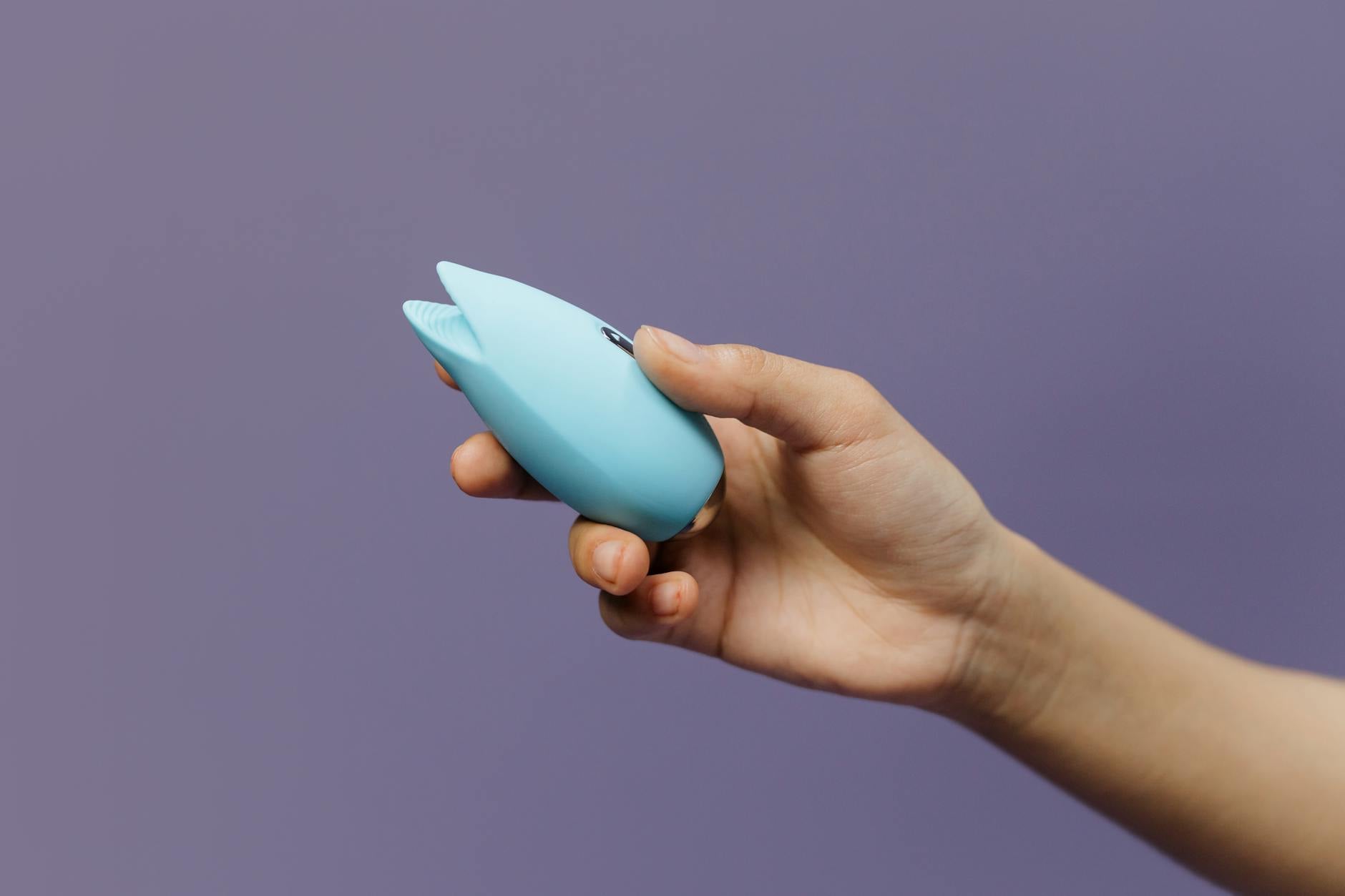 A silicone vibrator held gently in hand against a purple background